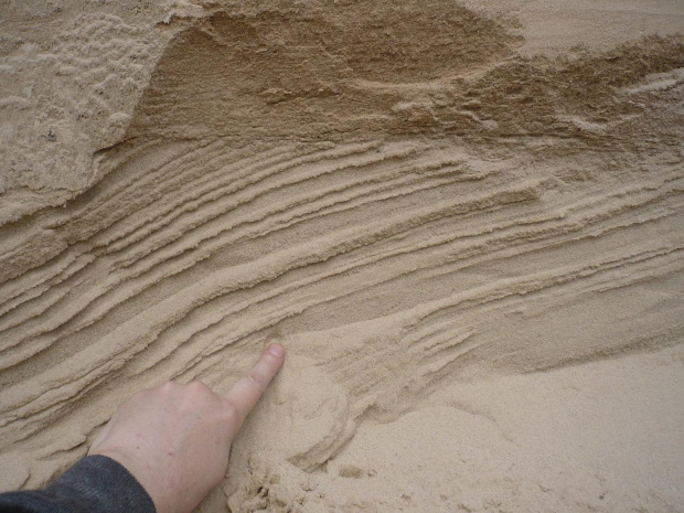 Piaski leżące podstawę okrywki. Widoczne dwie serie osadów piaszczystych. Warstwa niższa ma warstwowanie skośnym, świadczące o insttensywnym przepływie wody. Niższa, o warstwowaniu poziomym wskazuje na przepływ spokojniejszy.